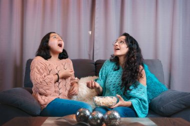 Evde film izleyen bir anne ve kızının yatay görüntüsü, ağızlarıyla yakalamak için patlamış mısır fırlatma oyunu oynuyorlar, çok komik ifadeler sergiliyorlar.