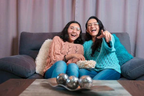Evde film izleyen bir anne ve kızın yatay görüntüsü, patlamış mısır yiyorlar, ikisi de çok komik gülüyor ve komik ifadeler takınıyorlar.