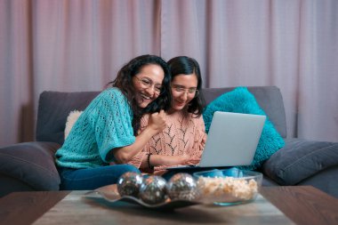 Bir annenin ve kızının dizüstü bilgisayar kullanırken yatay görüntüsü, kızı ona bilgisayarda bir şey gösteriyor ve annesi minnettarlık içinde kızına sarılıyor.