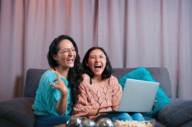 Bilgisayar ekranında gördüklerine kahkahalarla gülen bir anne ve kızın yatay görüntüsü.