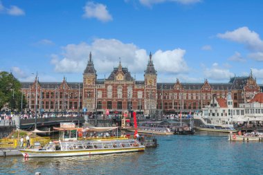 20 Ağustos 2025, Amsterdam, Hollanda. Sıcak bir yaz gününde arka planda Amsterdam Merkez İstasyonu ile sokaklarda yürüyorum..