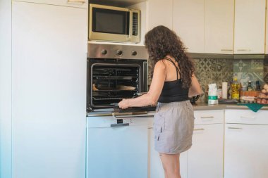 Mutfakta orta yaşlı bir kadın yemek pişiriyor, fırını açıyor, mutfakta kadın yemeğini çıkarmak için fırını açıyor..