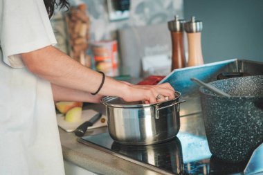 Elektrikli ocakta kaynatmak için tencereye sebze koyan genç bir kadının elleri, evde yemek pişirmek, sağlıklı yiyecek kavramı.