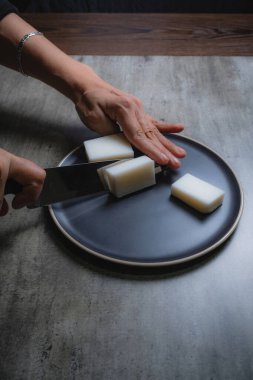 Evde, doğal banyo sabunu yapmak için organik sabun macunu kesen bir kadının ellerini görebilirsiniz. Ev yapımı. Yüzde yüz doğal..