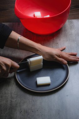 Evde, doğal banyo sabunu yapmak için organik sabun macunu kesen bir kadının ellerini görebilirsiniz. Ev yapımı. Yüzde yüz doğal..