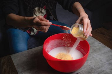 Evde, bir kadının elleri kırmızı bir kapta turuncu esanslı organik sabun karıştırırken görülebilir. Yüzde yüz doğal.