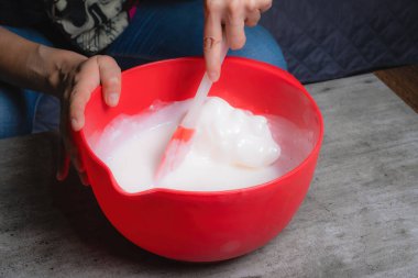 Evde, bir kadının elleri kırmızı bir kapta turuncu esanslı organik sabun karıştırırken görülebilir. Yüzde yüz doğal.