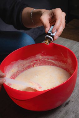 Evde, bir kadının elleri kırmızı bir kapta turuncu esanslı organik sabun karıştırırken görülebilir. Yüzde yüz doğal.