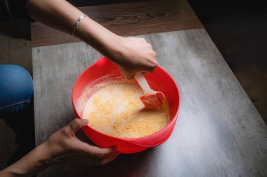 Evde, bir kadının elleri kırmızı bir kapta turuncu esanslı organik sabun karıştırırken görülebilir. Yüzde yüz doğal.