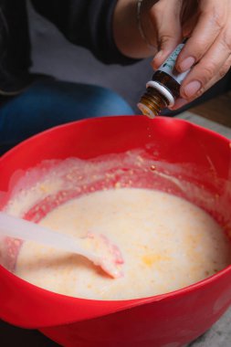 Evde, bir kadının elleri kırmızı bir kapta turuncu esanslı organik sabun karıştırırken görülebilir. Yüzde yüz doğal.