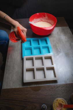 Evde, doğal sabunun silikon kaplara döküldüğü kırmızı bir kap tutan bir kadının ellerini görebilirsiniz. Sabun% 100 organik ve ev yapımı..