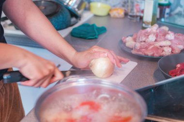 Orta yaşlı bir kadın soğan doğruyor ve onları kaynayan bir tencereye koyup ev yapımı yemekler hazırlıyor.