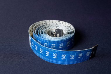 Soldan sağa aydınlatmalı koyu siyah arka planda metal uçlu mavi ve beyaz mezura. Kilo verme süreci, genel olarak ölçümler, sağlıklı yaşam ve dikiş.