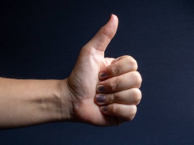 White woman's hand making a positive sign and approval gesture on a dark black background with light from right to left.