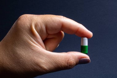 Green and white medicine capsules capsule in detail held by a white woman's hand on a black background. Used to strengthen the body and immunity, also as a food supplement.