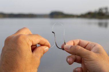 Beyaz bir adamın elleri gölün önündeki siyah bir oltanın gözüne naylon bir olta atıyor. Kıyı balıkçılığına, spora ve güneşli bir hafta sonunda ailenle geçirdiğin boş zamanlardan bahset..