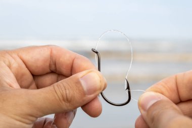 Beyaz bir adamın elleri denizin önündeki siyah bir oltanın gözüne naylon bir olta atıyor. Kıyı balıkçılığına, spora ve güneşli bir hafta sonunda ailenle geçirdiğin boş zamanlardan bahset..