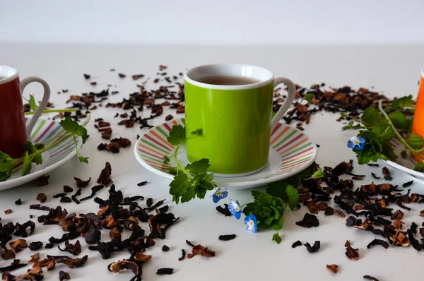 Zielona Filiżanka Białym Stole Liśćmi Kwiatami Białym Tłem Rozsypaną Herbatą — Zdjęcie stockowe