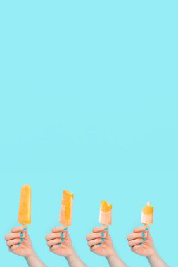 Bilinmeyen insanlar ellerinde mavi arka planda turuncu dondurma tutuyorlar. dikey resim