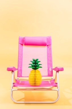 Sarı arka planda ananaslı pembe plaj koltuğu. Dikey görüntü. 3B illüstrasyon