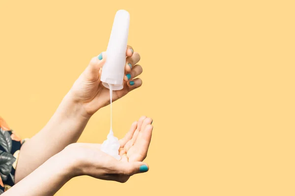 Hands of unknown woman with a tube applying cream on her hands on yellow background. Concept of cosmetic products. vertical image