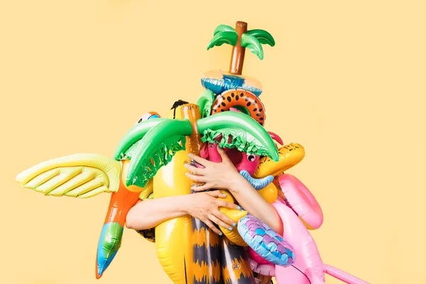 unknown person hugging a lot of pool inflatables of different shapes and colors on a yellow background