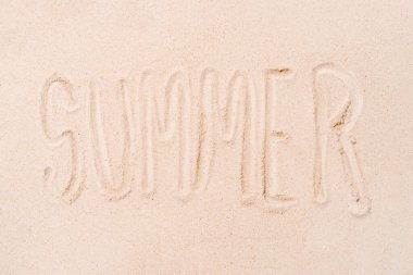 the word summer written with the finger on a sandy beach background. concept of summer and holidays. copy space.