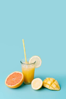 glass of fruit juice with straw to a fresh exotic fruit on blue background - mango, lemon, grapefruit. Concept of summer and healthy food. Vertical image with copy space