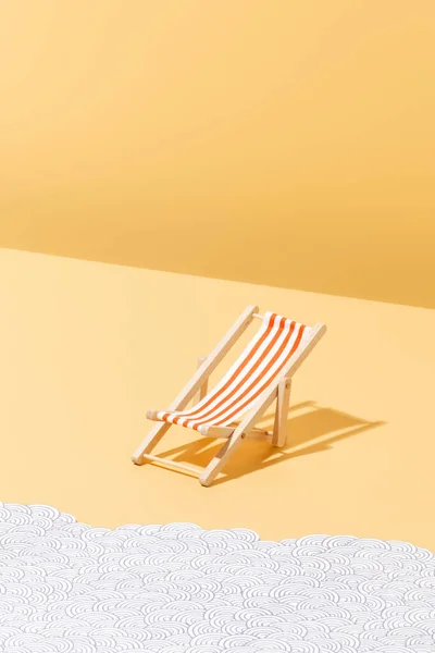 A red striped beach chair for sunbathing on a yellow background and paper waves Summer and holiday concept. vertical image with copy space