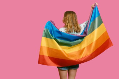 Sırtı dönmüş, elinde pembe bir arka planda gökkuşağı bayrağı olan beyaz, genç, sarışın bir kız. Gökkuşağı konsepti, LGBTQIA gay-lezbiyen gurur ve çeşitliliğinin sembolü..