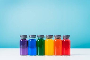 Beyaz ve mavi arka planda izole edilmiş gökkuşağı renkli sıvı cam şişeler. Aşı konsepti ve covid. Boşluğu kopyala