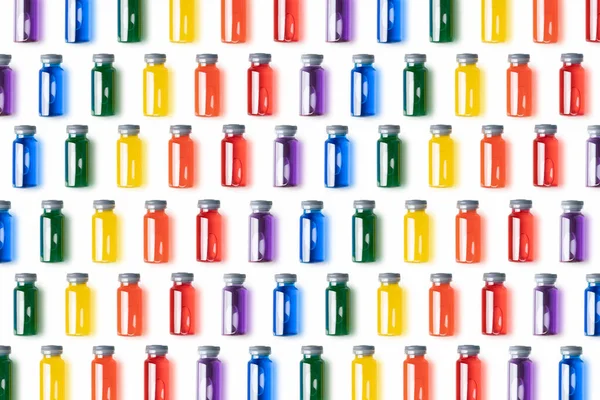 Beyaz zemin üzerinde gökkuşağı renkli sıvı bulunan cam şişelerin deseni. Aşı ve covid konsept..