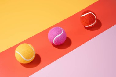 Renkli bir arkaplanda üç sarı, pembe ve turuncu tenis topu..