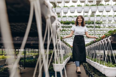 Çekici kadın çiçekçi, önlük giyiyor ve bahçe merkezinde ve saksılarda çalışıyor.