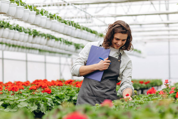 Крупный план. Молодой красивый цветочный мужчина наблюдает за цветами и делает заметки
