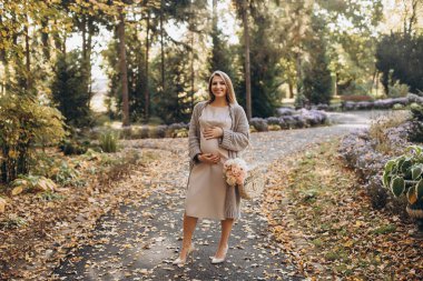 Parkta poz veren hamile bir kadın. Parkta yürüyordum. Profesyonel makyaj malzemesi. Mutlu ve tasasız hamilelik. Sonbahar parkı. Özgür mutlu kadın doğanın tadını çıkarıyor.