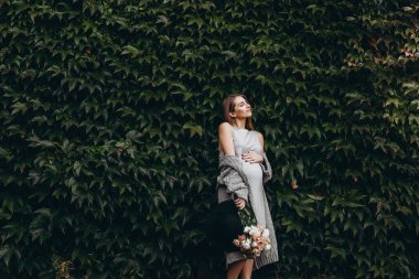 Yeşil yapraklardan bir duvar. Mutlu hamile kız gökyüzüne bakıyor..