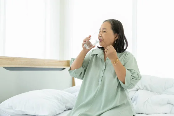 Senior woman drinking water on bed in the morning.