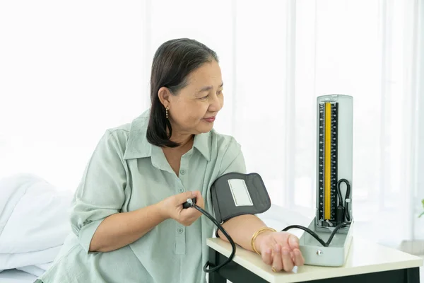 Senior woman measures blood pressure on her left hand with a digital blood pressure monitor.