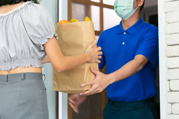 Asian deliver man wearing face mask in blue uniform and express grocery delivery service during covid19.