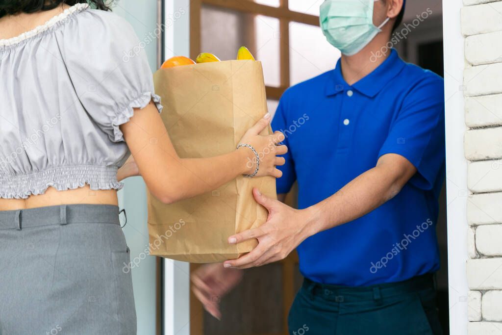 Asian deliver man wearing face mask in blue uniform and express grocery delivery service during covid19.