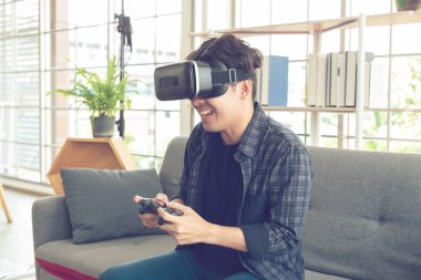 Sanal gerçeklik kulaklığı olan mutlu genç bir adam ya da evde video oyunu oynayan kontrol paneli olan 3D gözlükler..
