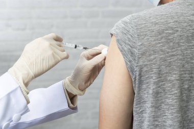 Virüs hastalığından korunmak için koruyucu maske takan doktor hastaya aşı enjekte ediyor..