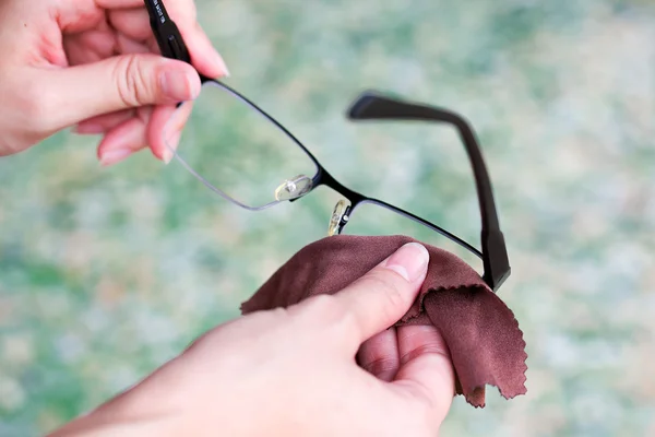 Women hand cleaning glasses lens with blur green background.. Stock Picture