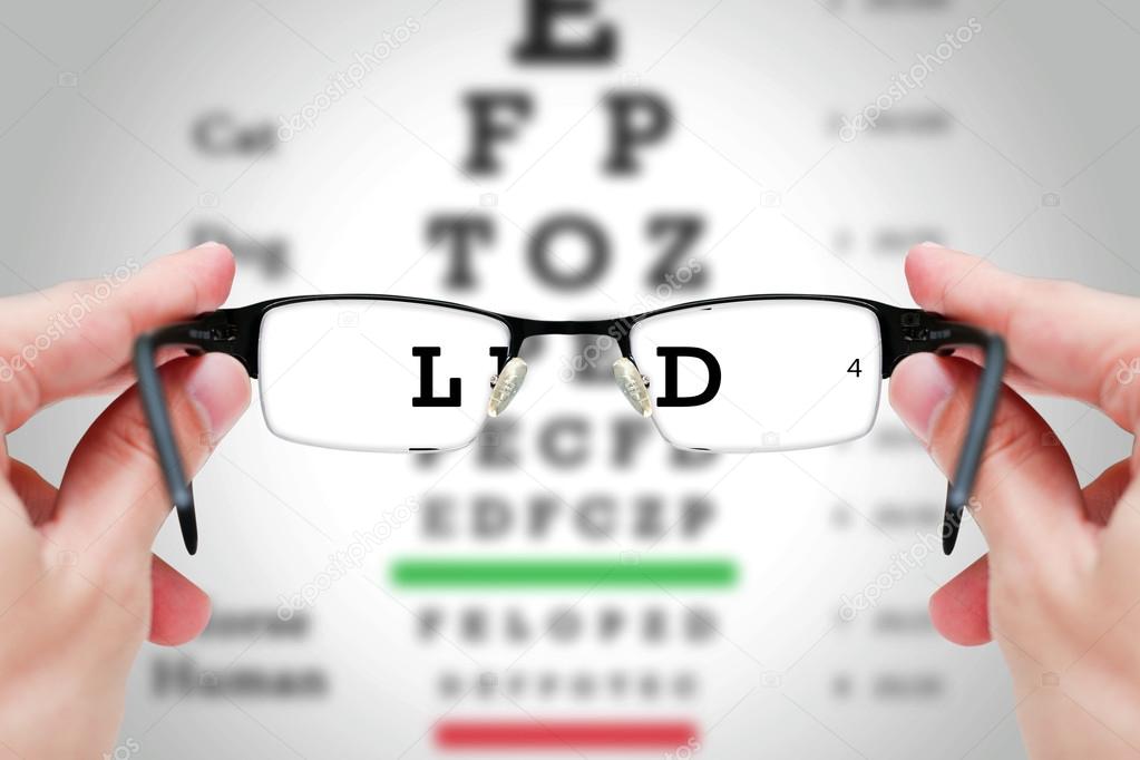 Female hand holding glasses with eyesight test on chart board.