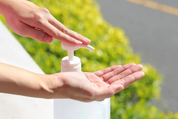 Female using gel sanitizer with green healthy blurry background. — Stock Photo, Image