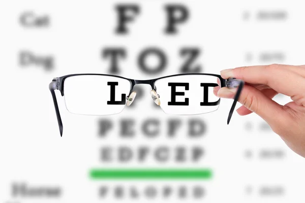 Female hand holding glasses with eyesight test on chart board. — Stock Photo, Image