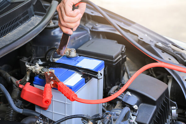 Car mechanic uses battery jumper cables charge a dead battery.