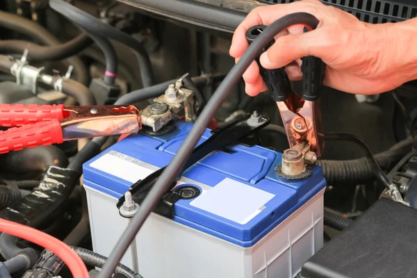 Car mechanic uses battery jumper cables charge a dead battery. Royalty Free Stock Photos
