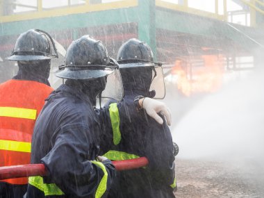 Firefighters fighting fire with pressured water during training exercise. Fire fighter spraying a straight steam into fire off. clipart
